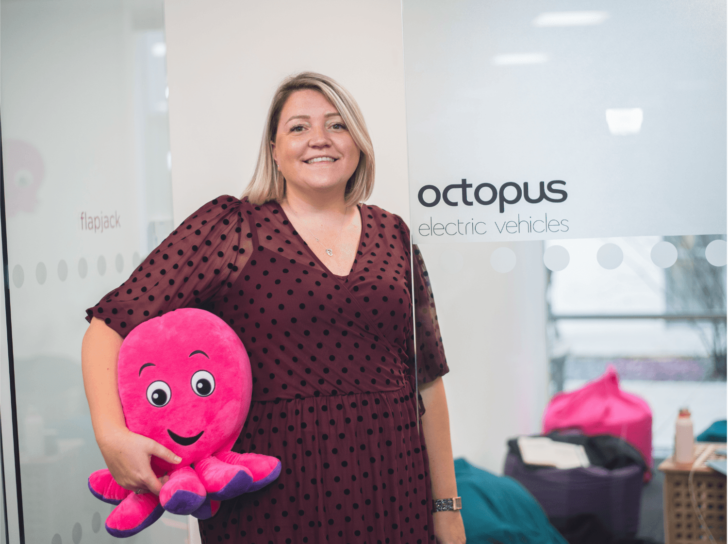 A woman holding a pink octopus toy in front of an Octopus Electric Vehicles sign